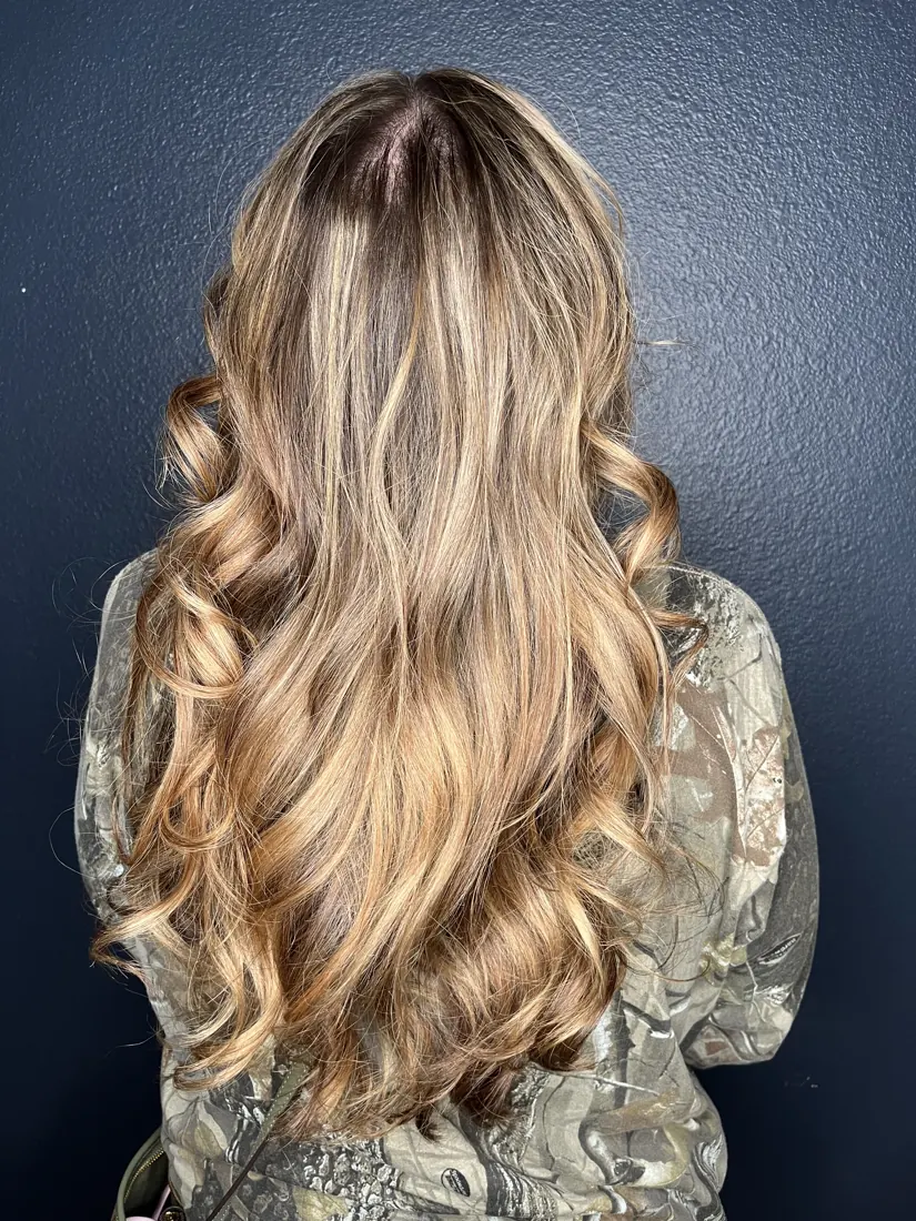 Rooted blonde balayage with soft curls against a navy wall